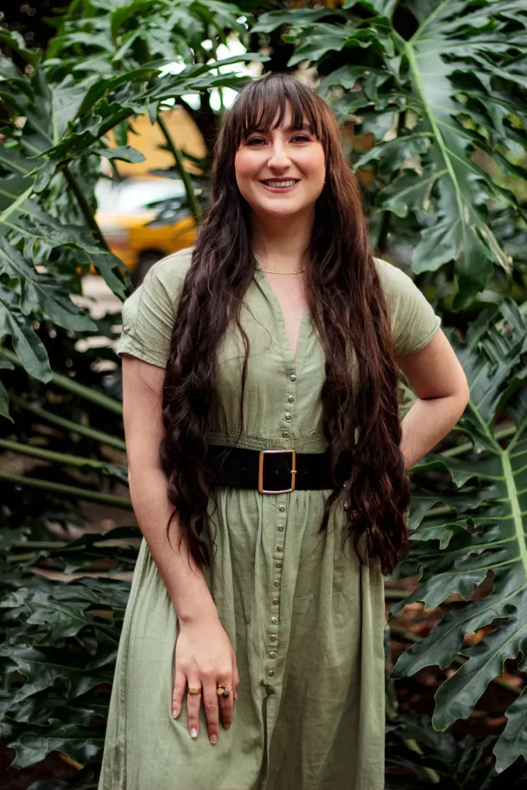 Ányela Márquez, directora de Oikos, sonríe de pie entre plantas de hojas grandes.