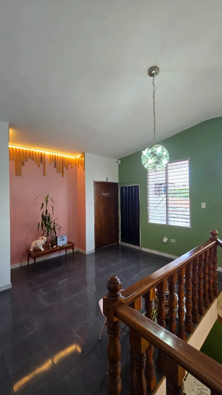 La planta alta: pared rosa con listones de madera iluminados, pared verde, una lámpara de cristal y la baranda de la escalera.