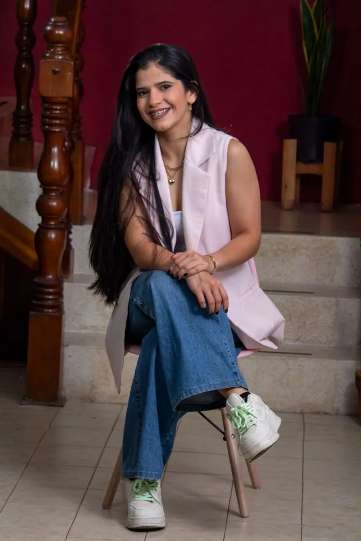 Jimberlyn Rivas sentada en una silla rosada junto a la escalera de Oikos, con chaleco rosado y jeans.